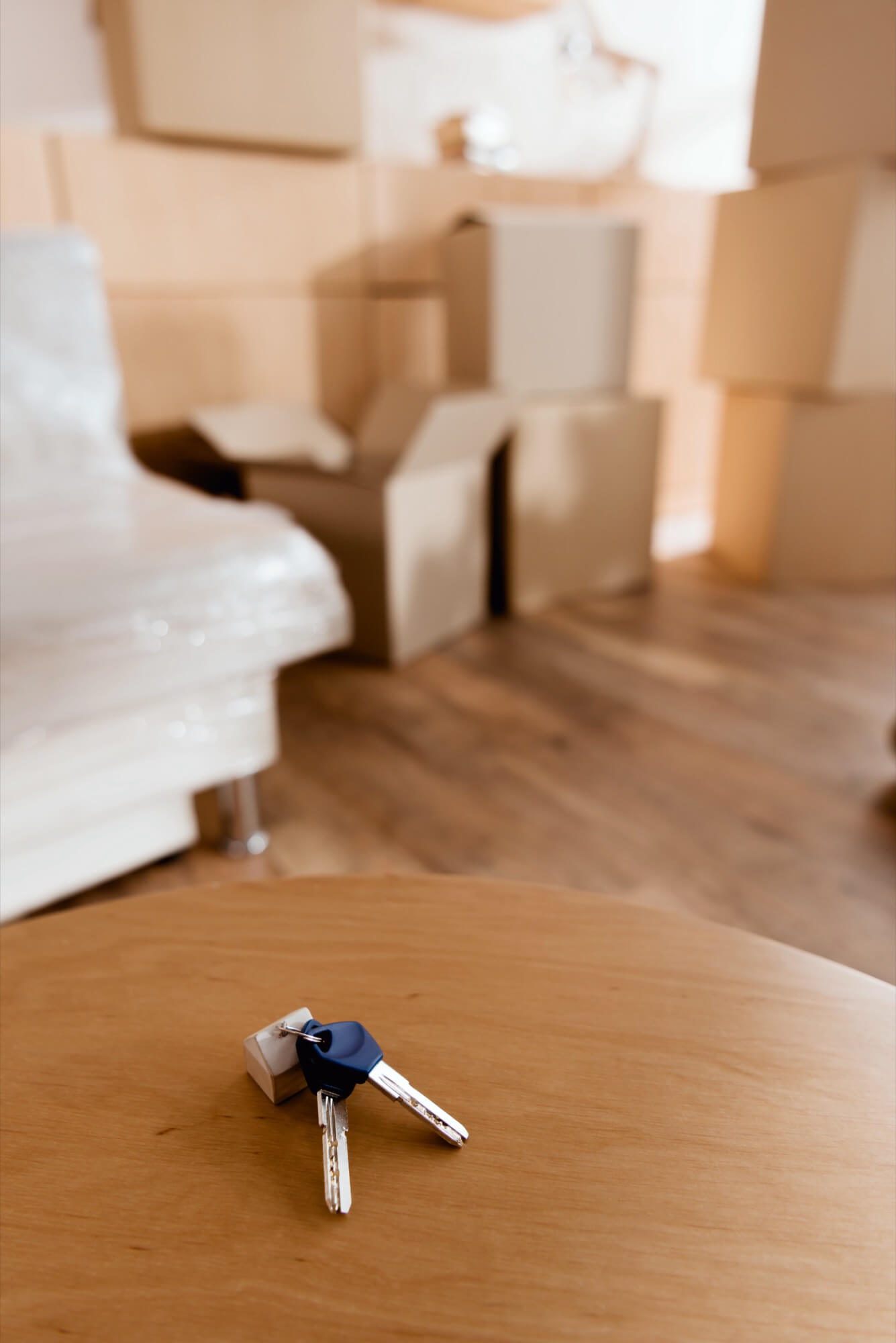 A pair of keys lies on a table with blurry moving boxes in the background, symbolizing moving into a new home.